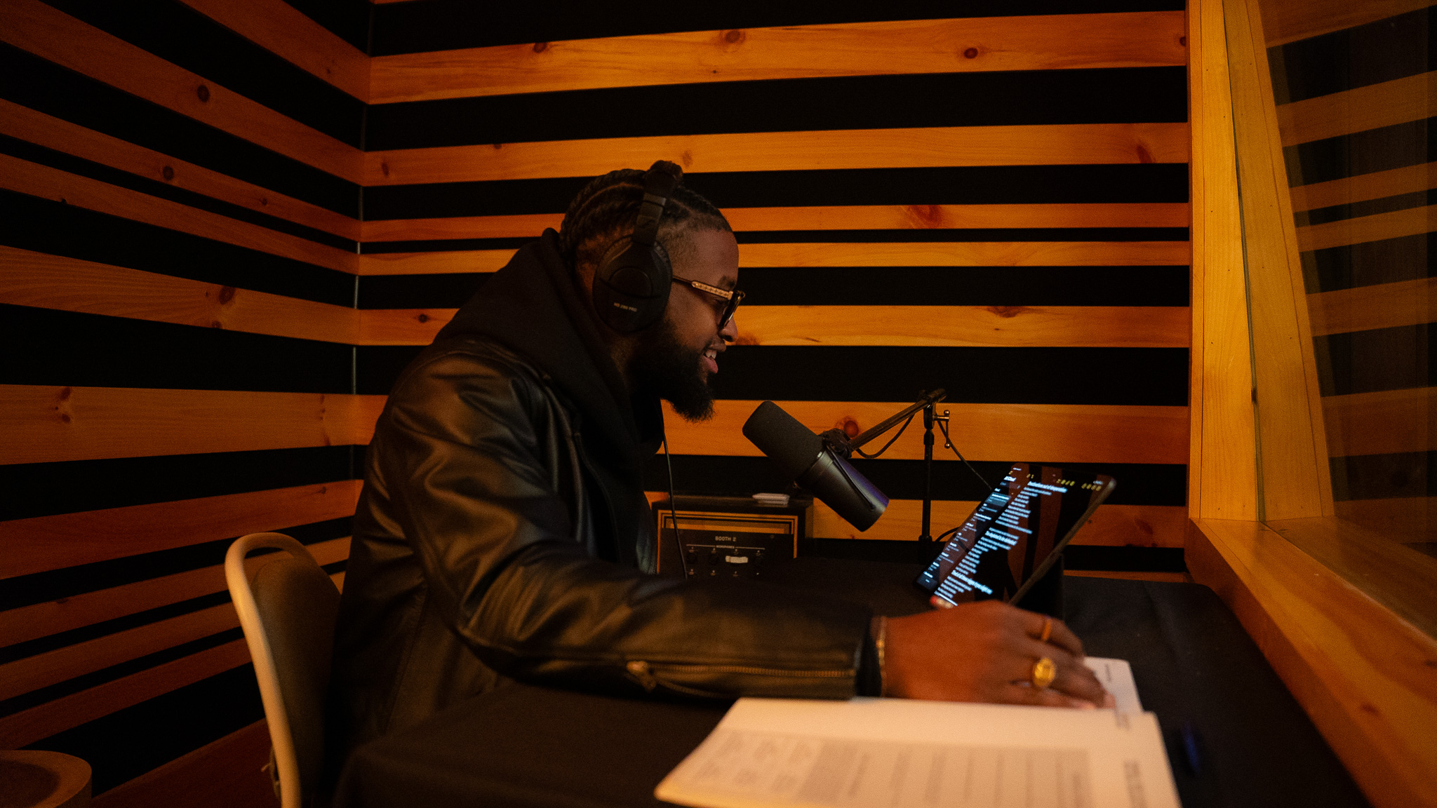Podcaster in leather jacket recording in wood-stripe booth